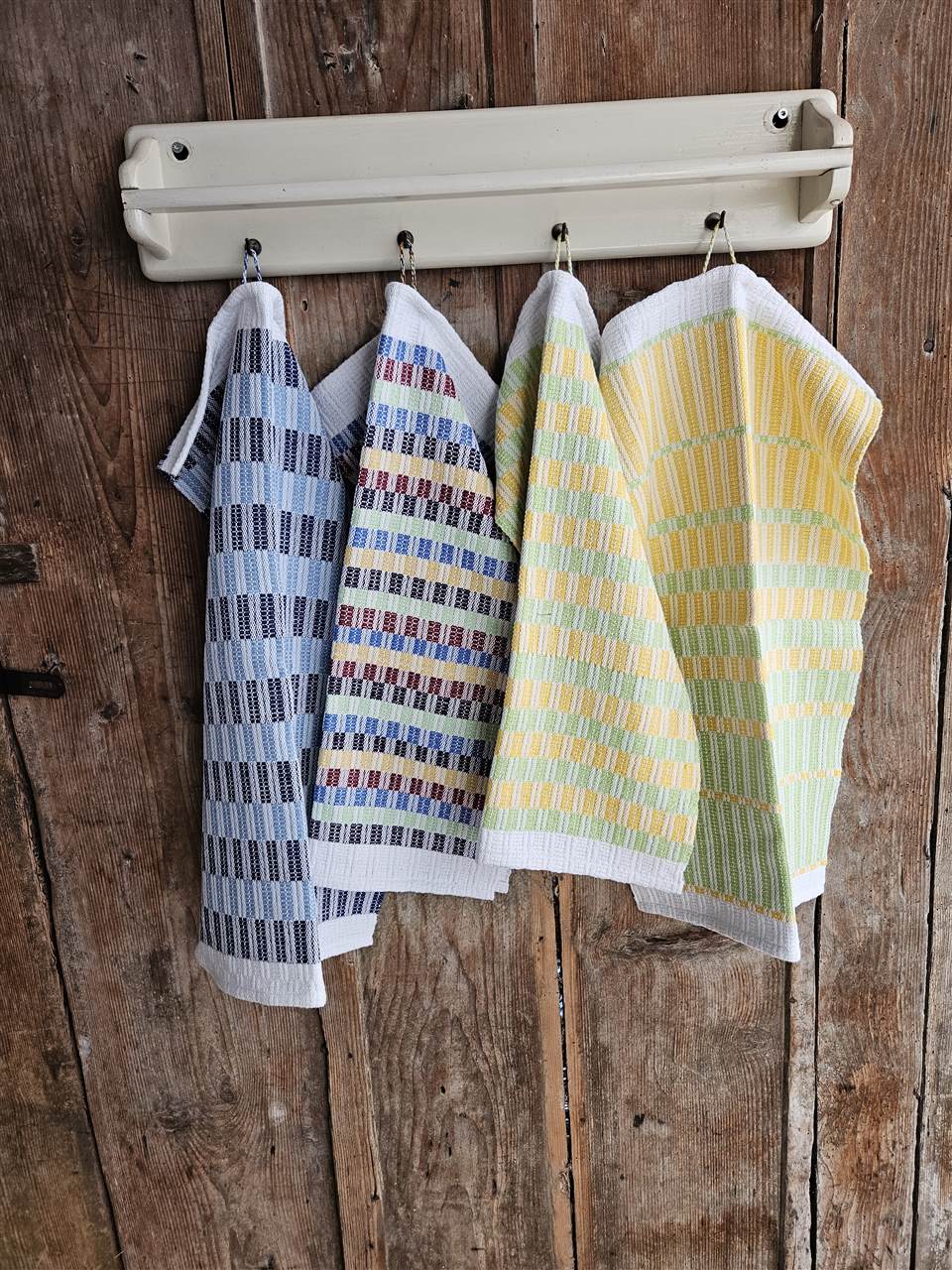 Handgewebte Tücher mit blauen, bunten und gelb-grünen Karos an einer Hakenleiste